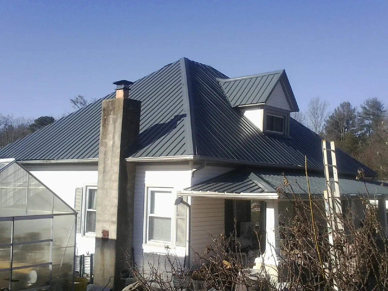 Dark blue standing seam metal roof on a white farmhouse with dormer in Industry