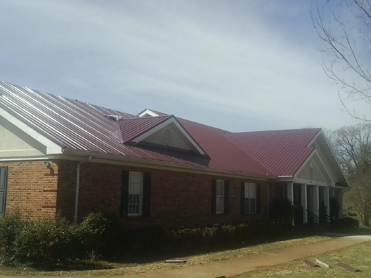 Red metal roof with gabled entries on a long brick building, from a Hail Damage Roof Repair job in Industry