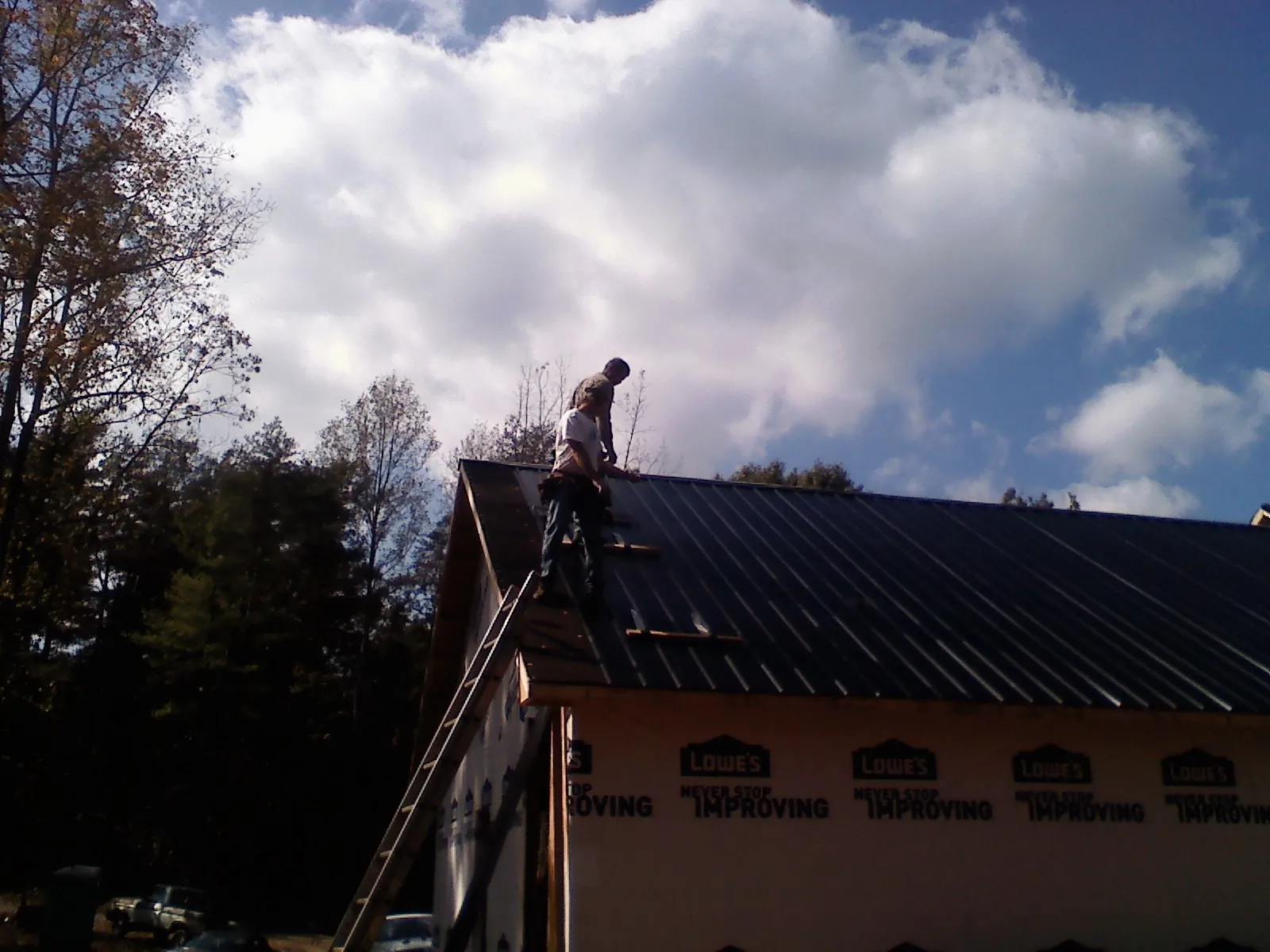 Roofer fastening dark metal panels high against a cloudy sky, from a Roof Inspection job in Industry